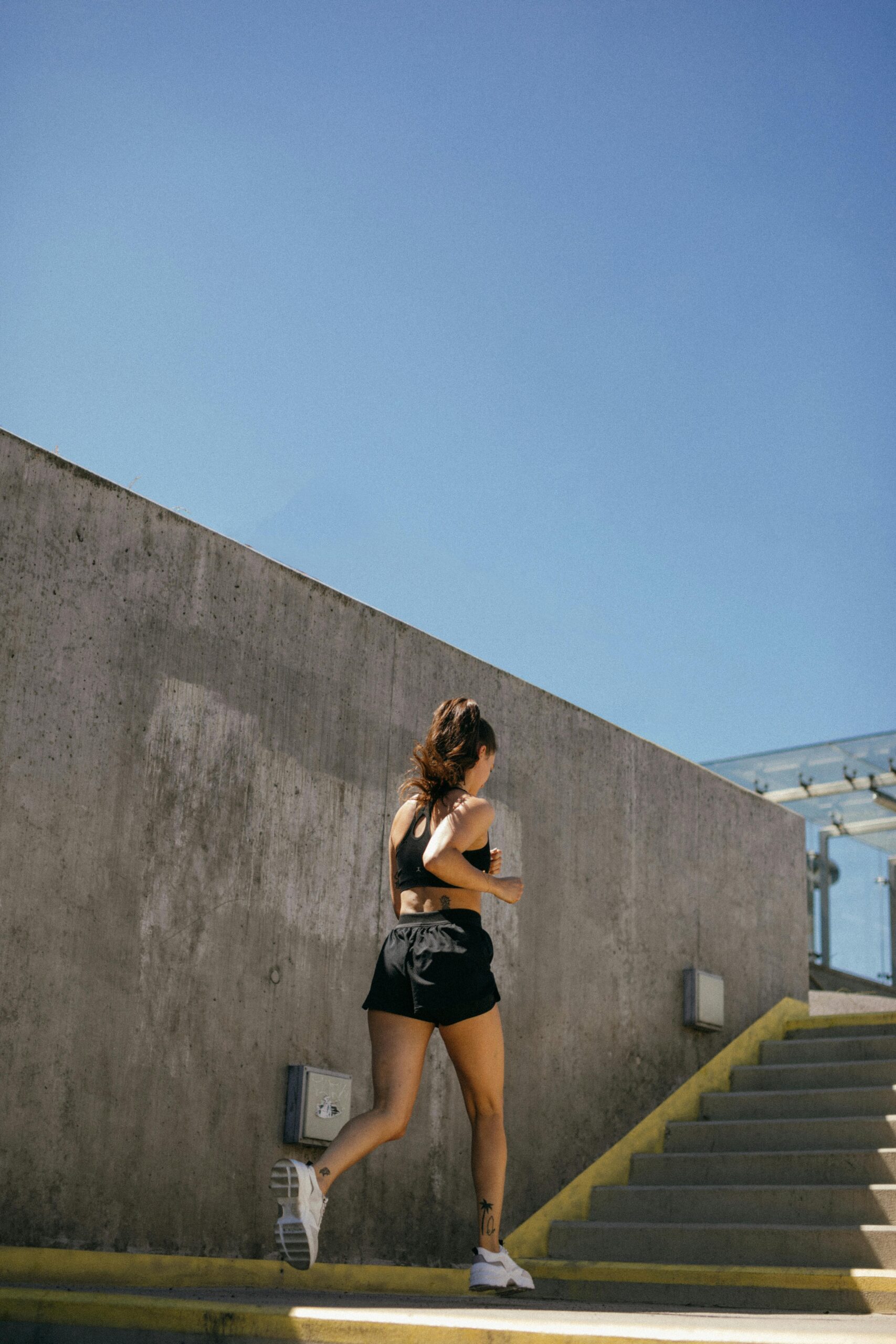 Fit woman running up outdoor stairs in sunny weather, showcasing athleticism and health.