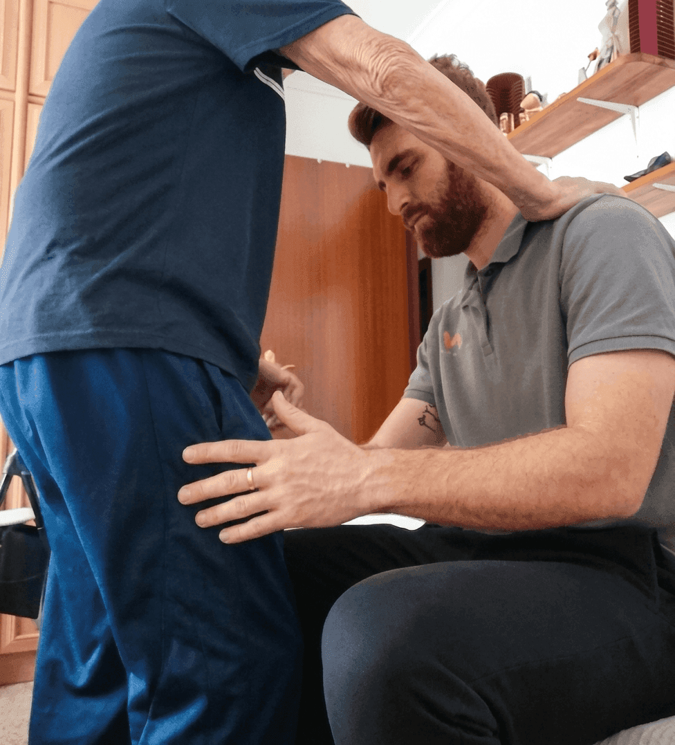 Fisioterapeuta de MVFisioHome trabajando el reentrenamiento del equilibrio y la marcha con un paciente en el pasillo de su domicilio
