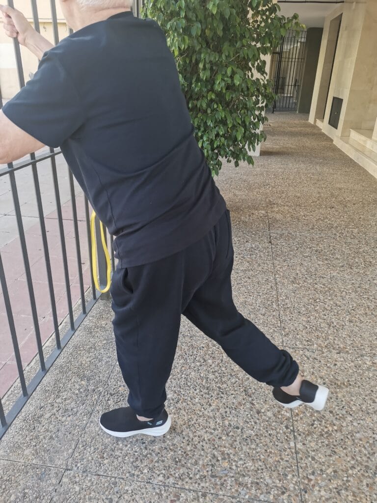 Paciente realizando ejercicio de extensión de pierna para fortalecer el glúteo en su domicilio de Sevilla, supervisado por el fisioterapeuta de MVFisioHome para mejorar la estabilidad y la marcha.