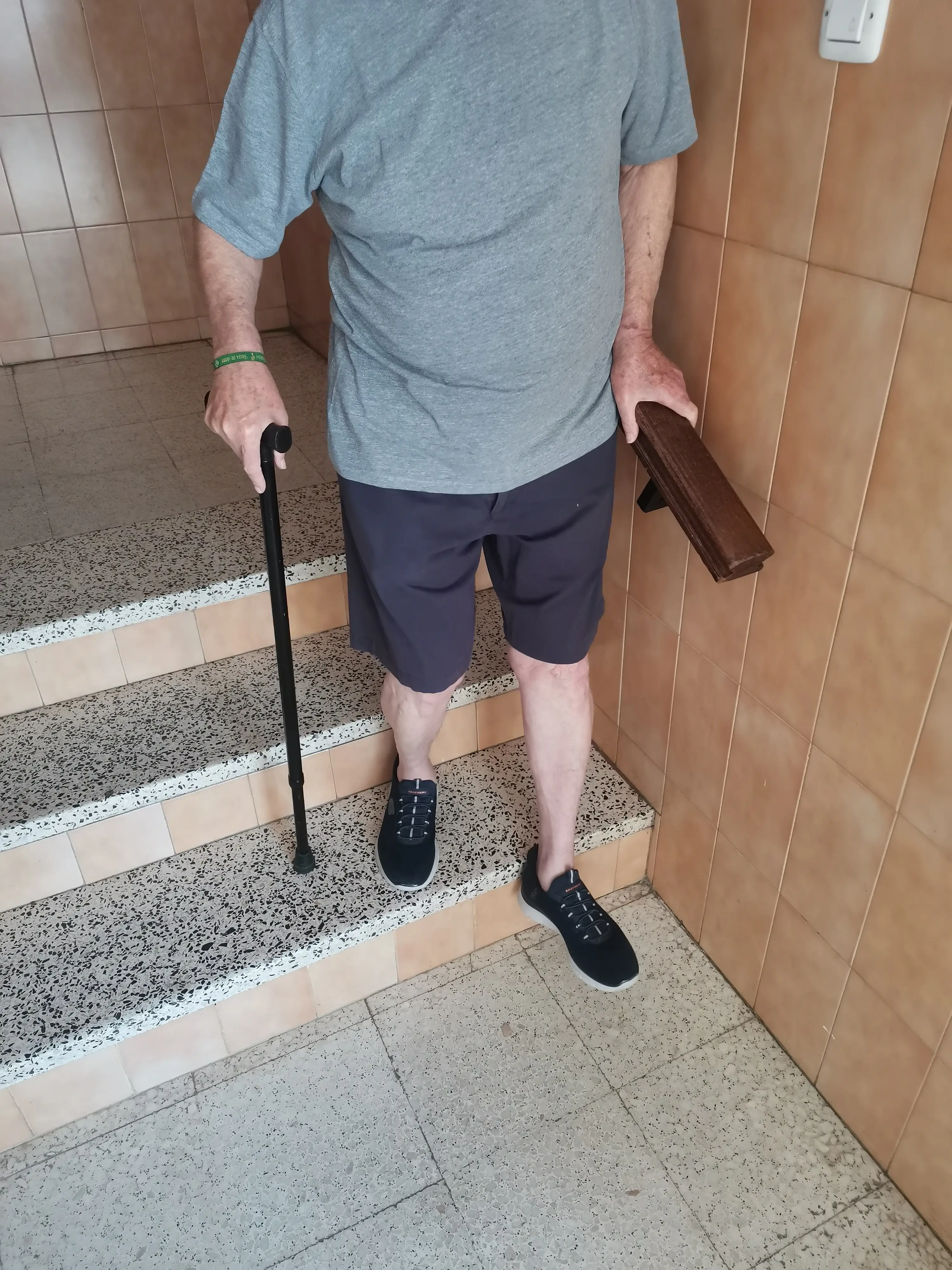 Paciente neurológico realizando reeducación de la marcha y bajando escaleras con bastón durante una sesión de fisioterapia a domicilio en Sevilla.